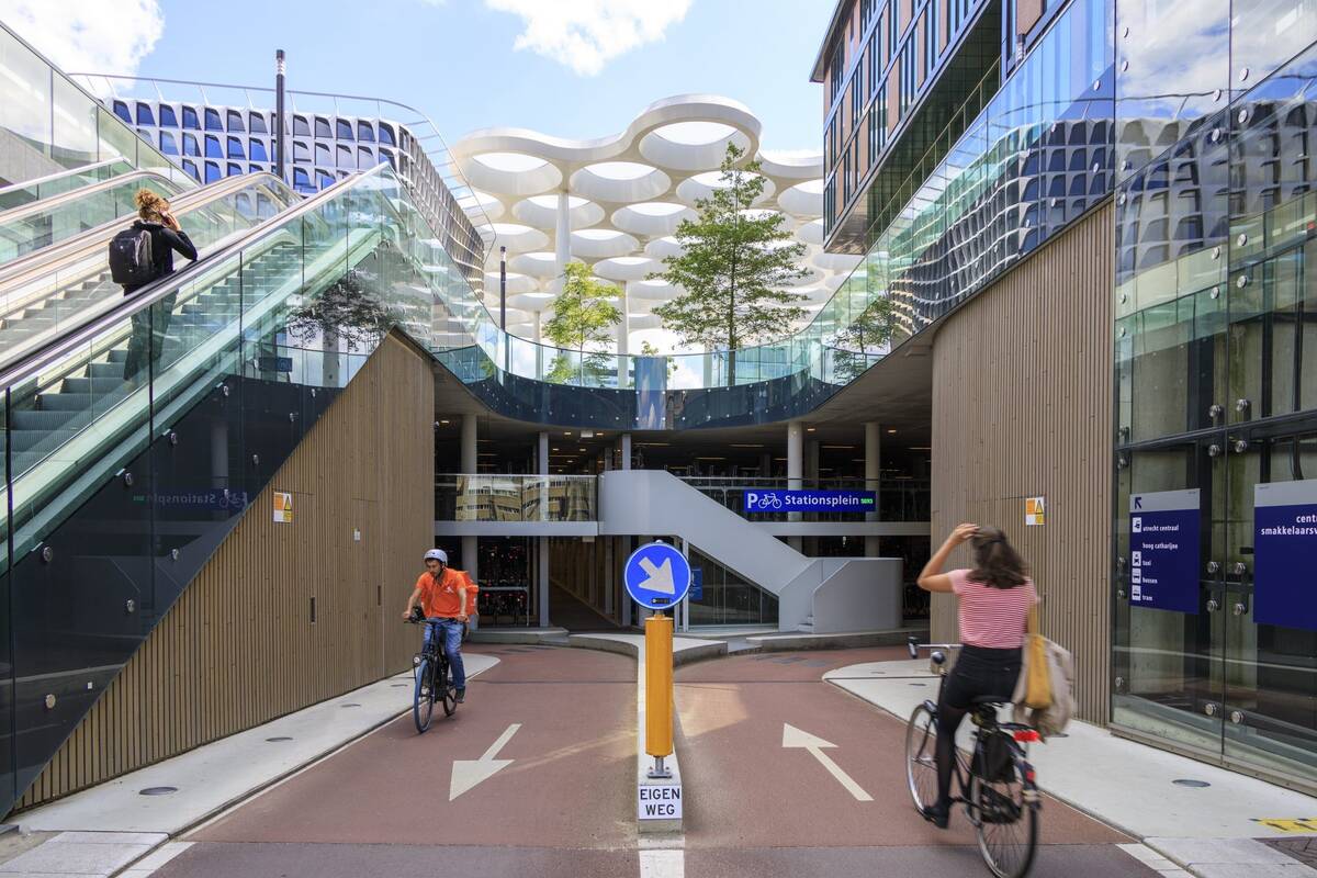 At the entrance of the largest bicycle shed in the world, a number of people cycle and walk.